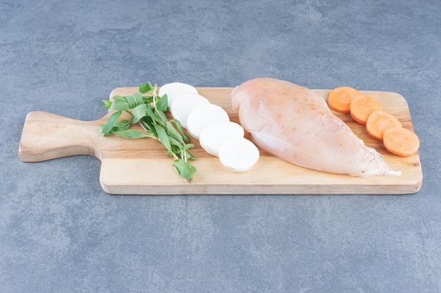 木の板に野菜を添えた未調理の鶏の切り身。