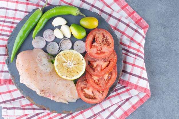 Сырое куриное филе на деревянной доске с овощами.