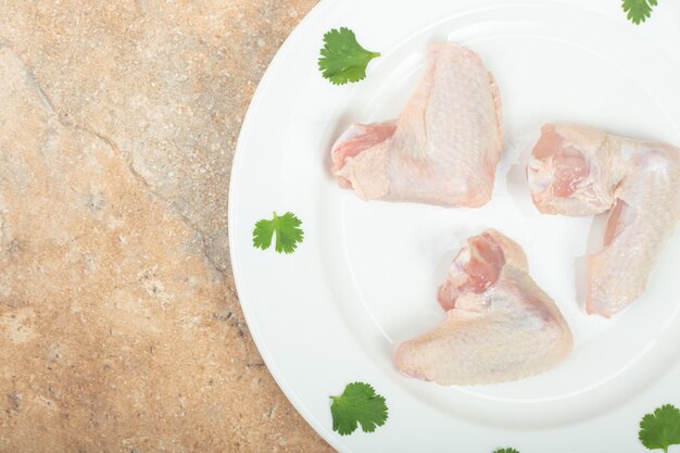 Uncooked chicken leg with greens on white plate