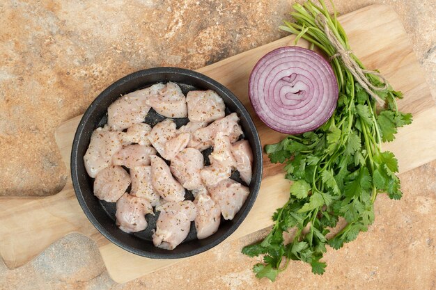 Uncooked chicken legs in dark pan with sliced onion .