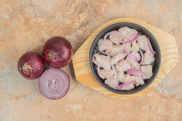 Uncooked chicken legs in dark pan with sliced onion