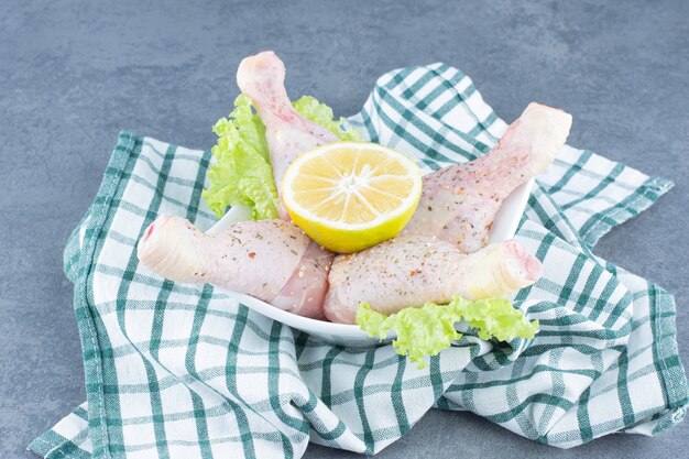 未調理の鶏の脚とレモンスライスを白いボウルに入れます。