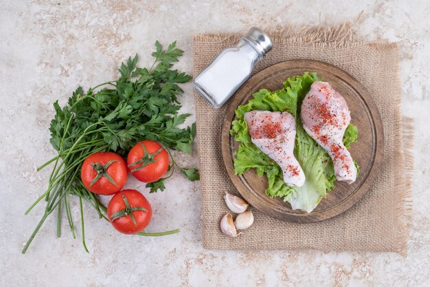 Uncooked chicken legs meat with vegetables on a wooden board