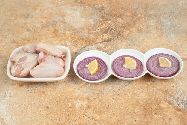 Uncooked chicken legs in white plate with sliced onion