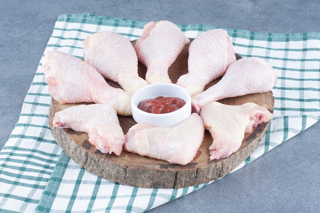 Uncooked chicken legs and wings on wood piece.