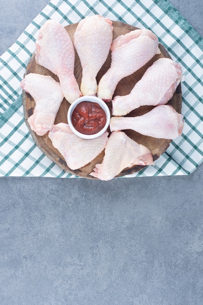 Uncooked chicken legs and wings on wood piece.