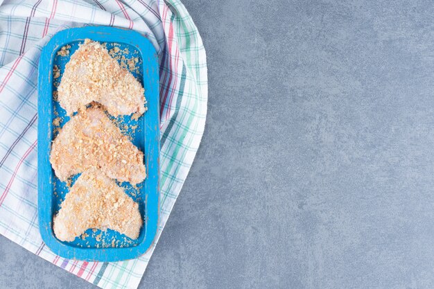 Uncooked chicken wings with bread crumbs on blue plate.