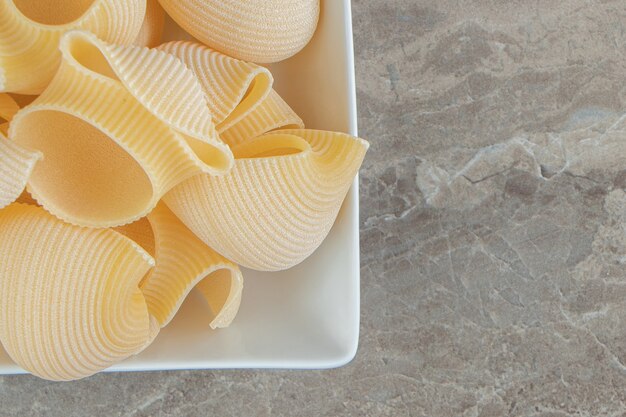 Uncooked conchiglie pasta in white bowl