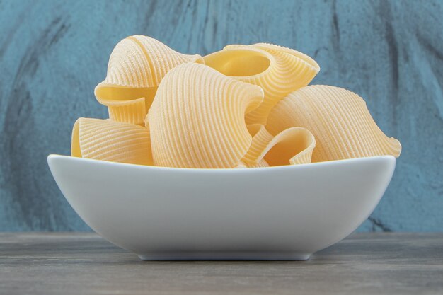 Uncooked conchiglie pasta in white bowl.
