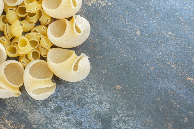 Сырые и приготовленные макароны в миске на мраморной поверхности.