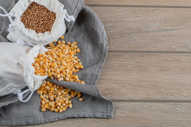 Uncooked corn grains and buckwheat on a wooden table.