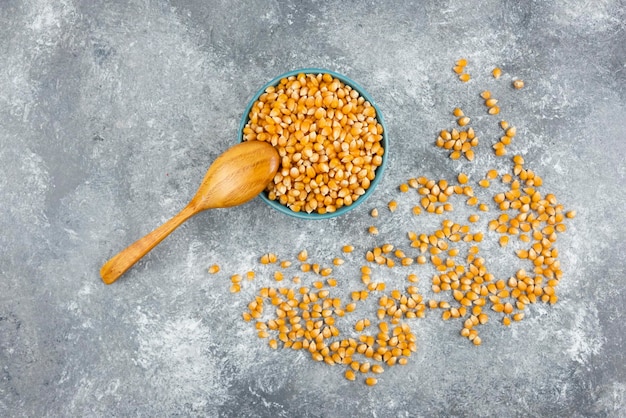 Uncooked corn kernels in blue bowl with wooden spoon.