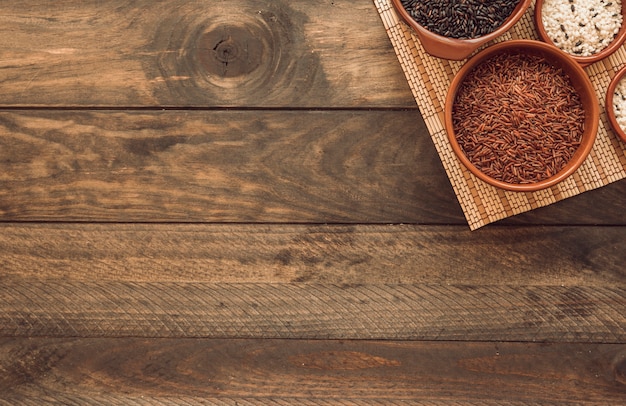 Uncooked different rice bowls on placemat over the wooden background