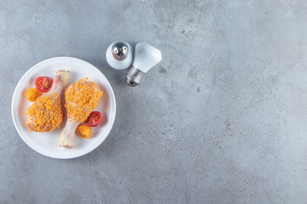 Uncooked drumsticks on a plate next to salt , on the marble background.