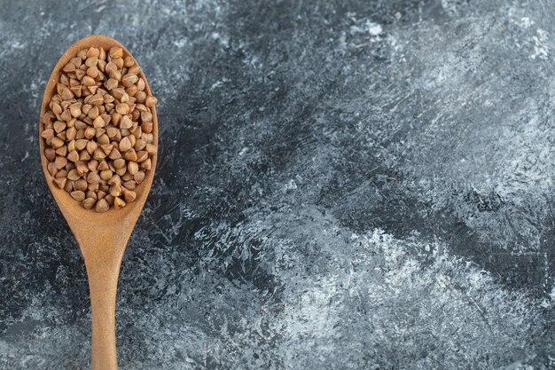 Uncooked dry buckwheat on wooden spoon