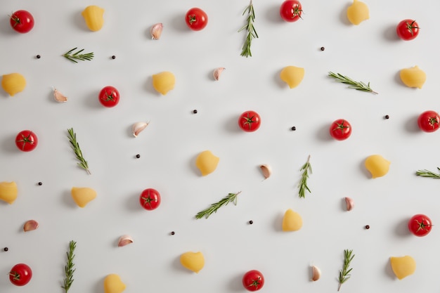 Uncooked dry whole pasta shells and fresh ingredients red tomatoes, pepper and rosemary. Trying best recipe for traditional Italian pasta. White background. View from above. Flat lay composition