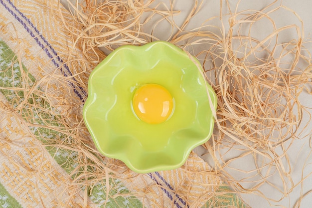 Бесплатное фото Сырое яйцо в зеленой тарелке с сеном на мраморном столе.