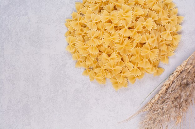 Uncooked farfalle pasta on white surface with wheat