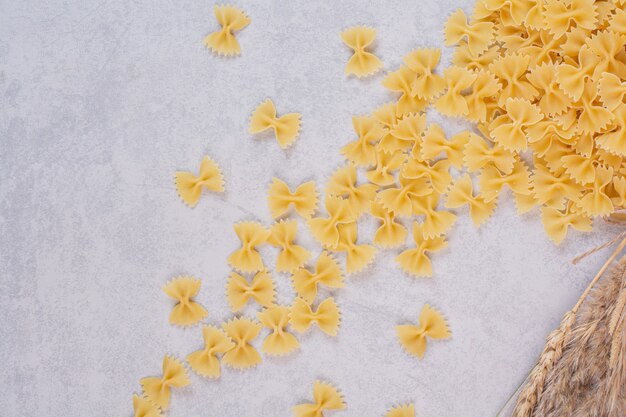 Uncooked farfalle pasta on white surface with wheat