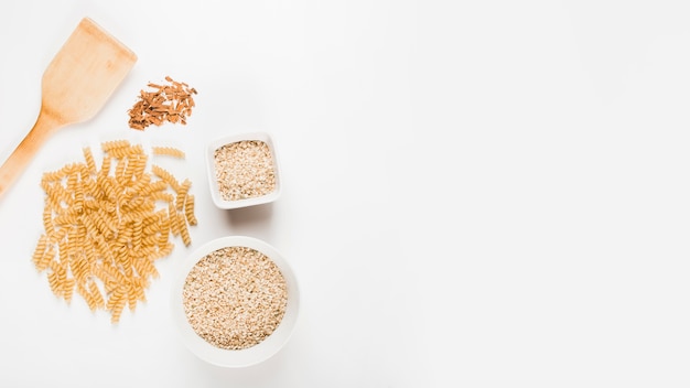 Uncooked fusilli pasta; rice and crushed cinnamon with spatula on white background