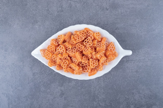 Uncooked heart-shaped pasta on leaf-shaped plate.