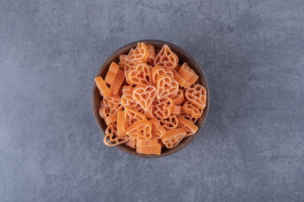 Uncooked heart-shaped pasta in wooden bowl.