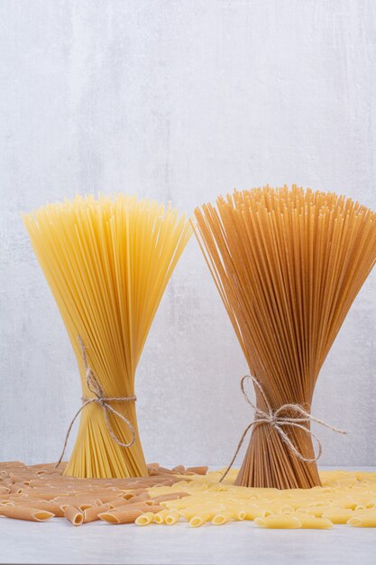 Uncooked macaroni with fresh raw pasta on white surface
