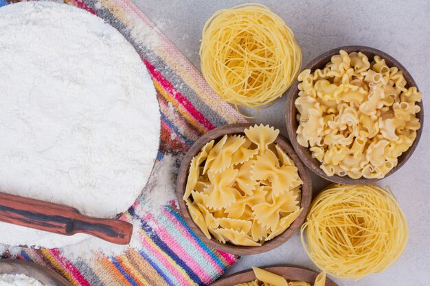 Free photo uncooked macaroni on wooden bowls with yolk and flour