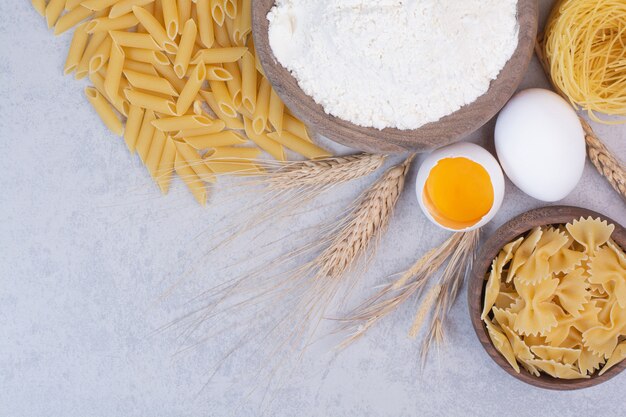 Uncooked macaroni on wooden bowls with yolk and flour. 