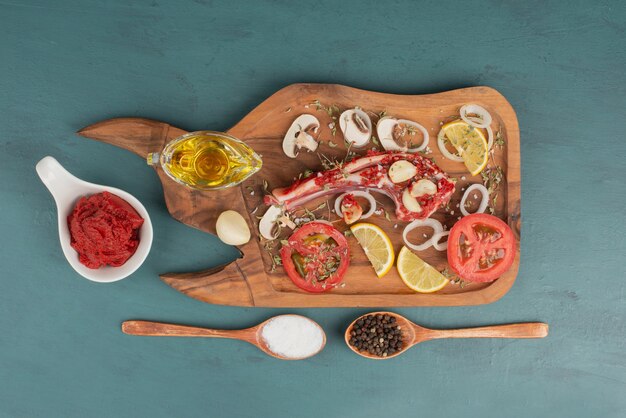 o 기름과 토마토 페이스트 옆에 파란색 테이블에 야채와 함께 생 쌀된 고기 조각.