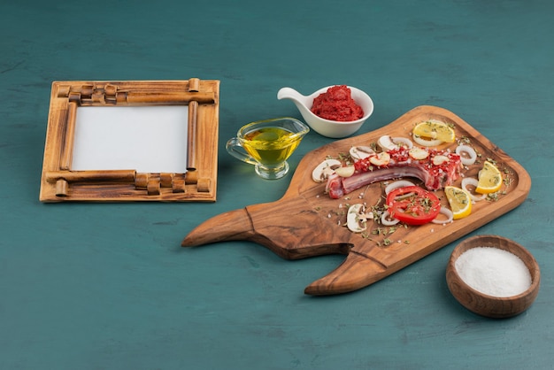 Free photo uncooked meat piece with vegetables and picture frame on blue table.