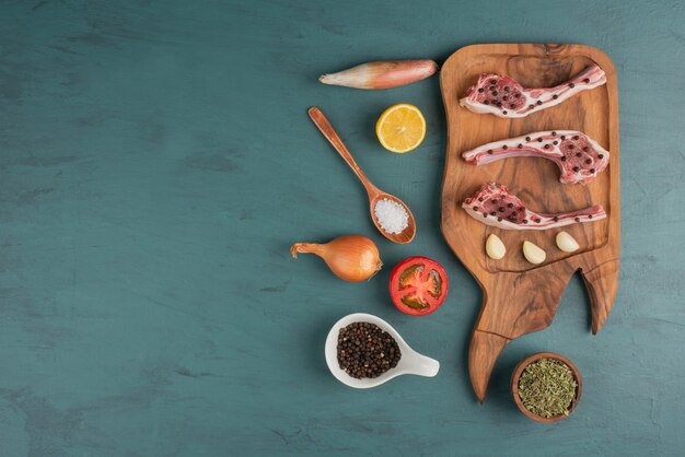 Uncooked meat pieces with vegetables, oil and spices on blue table.