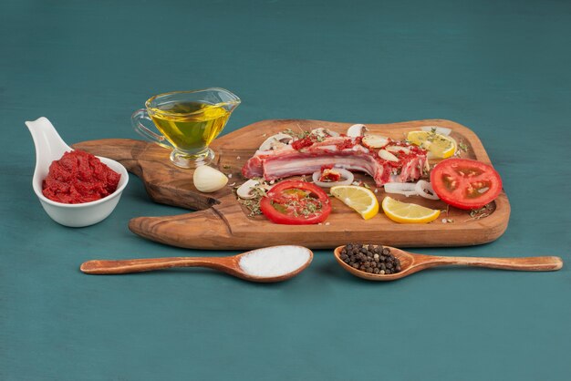 Кусочки сырого мяса с овощами, маслом и специями на синем столе.