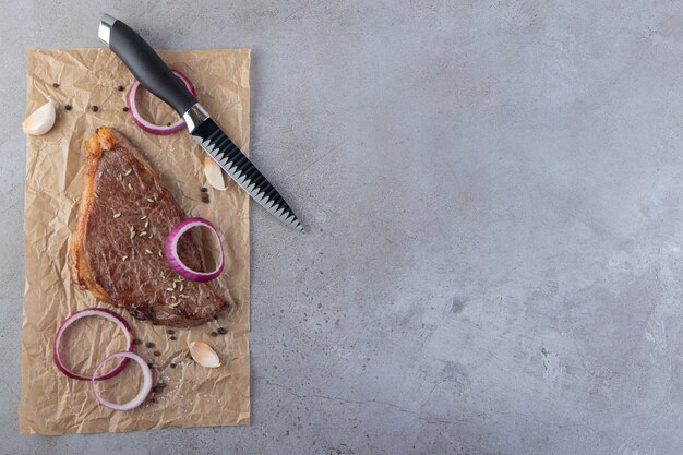 Uncooked meat with sliced onion and red cherry tomatoes placed on stone background.