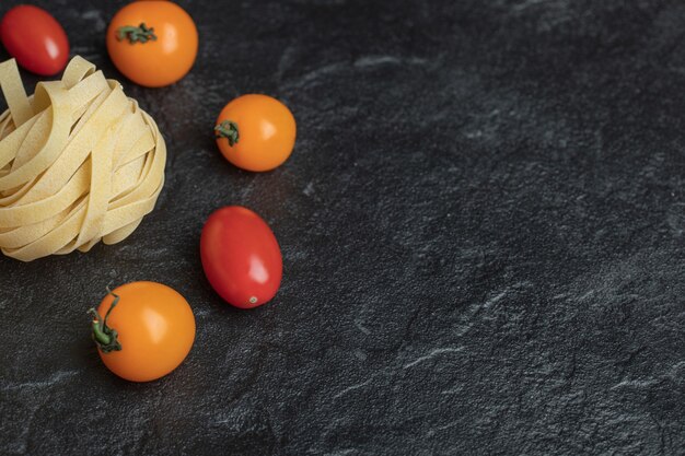 Uncooked nest pasta with cherry tomatoes on black.