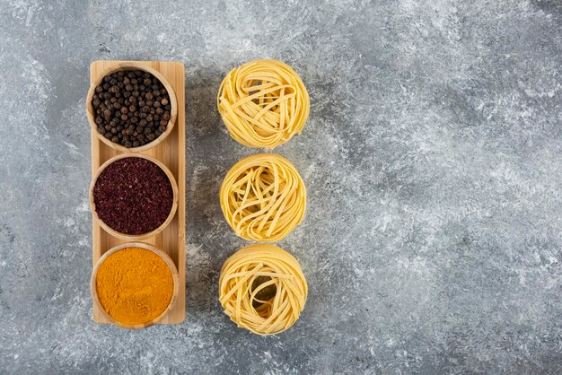 Uncooked nest pasta with spices on a gray table.