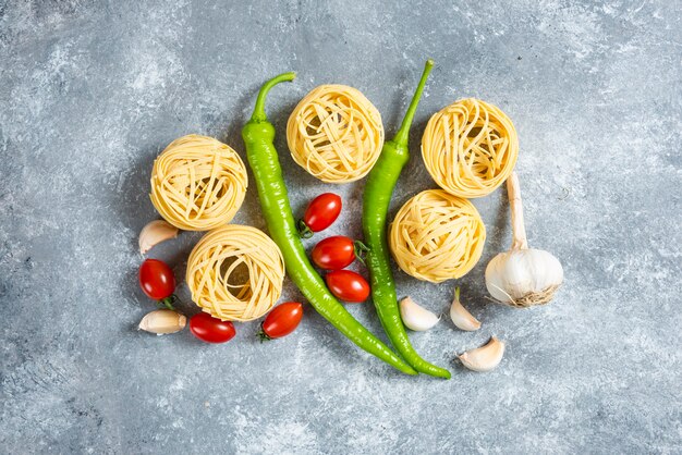 Uncooked nest spaghetti with vegetables on a marble background