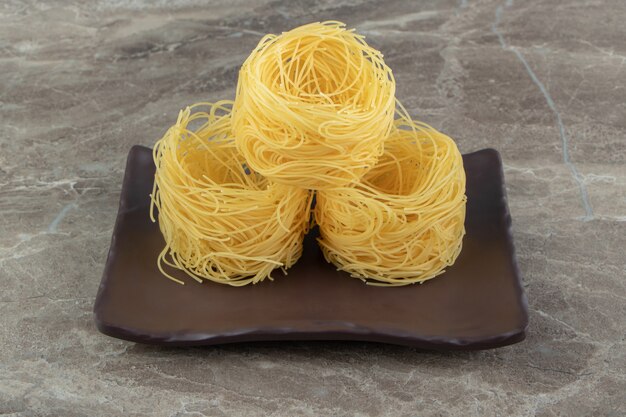 Uncooked noodle nests on dark plate