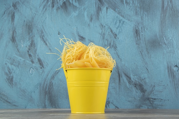 Free photo uncooked noodle nests and penne in yellow bucket