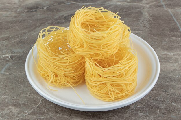 Uncooked noodle nests on white plate.