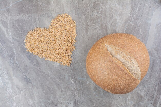 Uncooked oat grains with loaf of bread on marble surface
