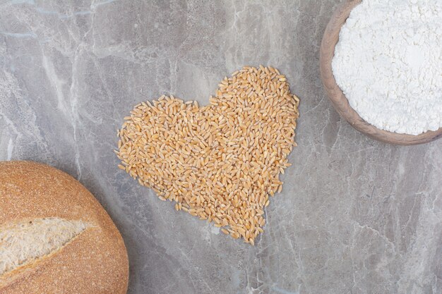 Uncooked oat grains with loaf of bread on marble surface