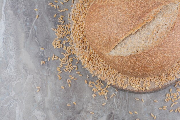 Uncooked oat grains with loaf of bread on marble surface