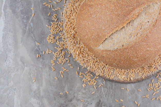 Бесплатное фото Сырые овсяные зерна с буханкой хлеба на мраморной поверхности