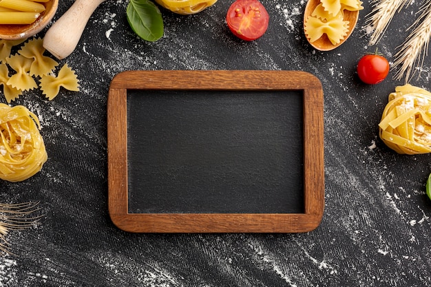 Free photo uncooked pasta arrangement frame on black background with wooden frame