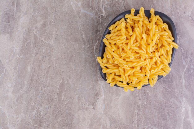 Uncooked pasta in a black ceramic bowl on the marble. 