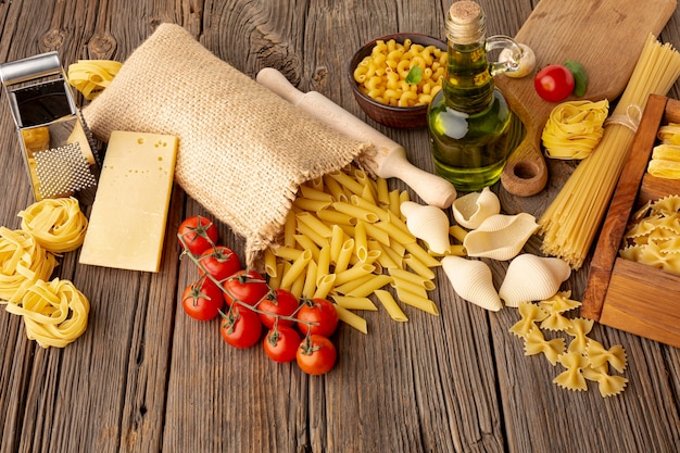 Free photo uncooked pasta mix with tomatoes olive oil and hard cheese