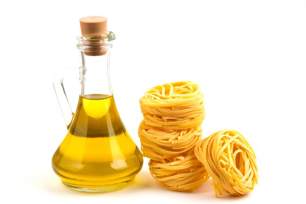 Uncooked pasta nests and bottle of oil on white.