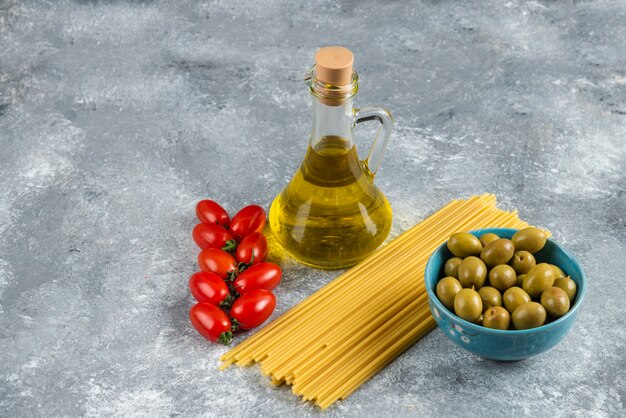 Uncooked pasta, oil and fresh vegetables on stone.