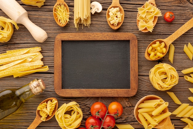 Free photo uncooked pasta olive oil and tomatoes with blackboard mock-up